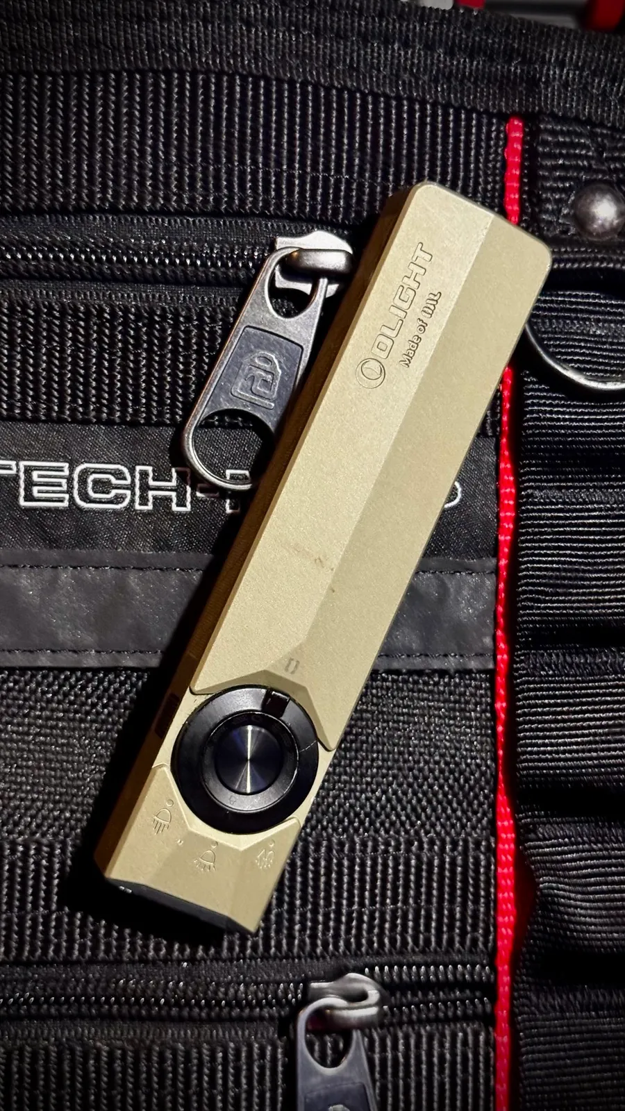The Olight ArkPro Ultra clipped vertically to the webbing of a black tool bag, showing how flat it sits against the panel