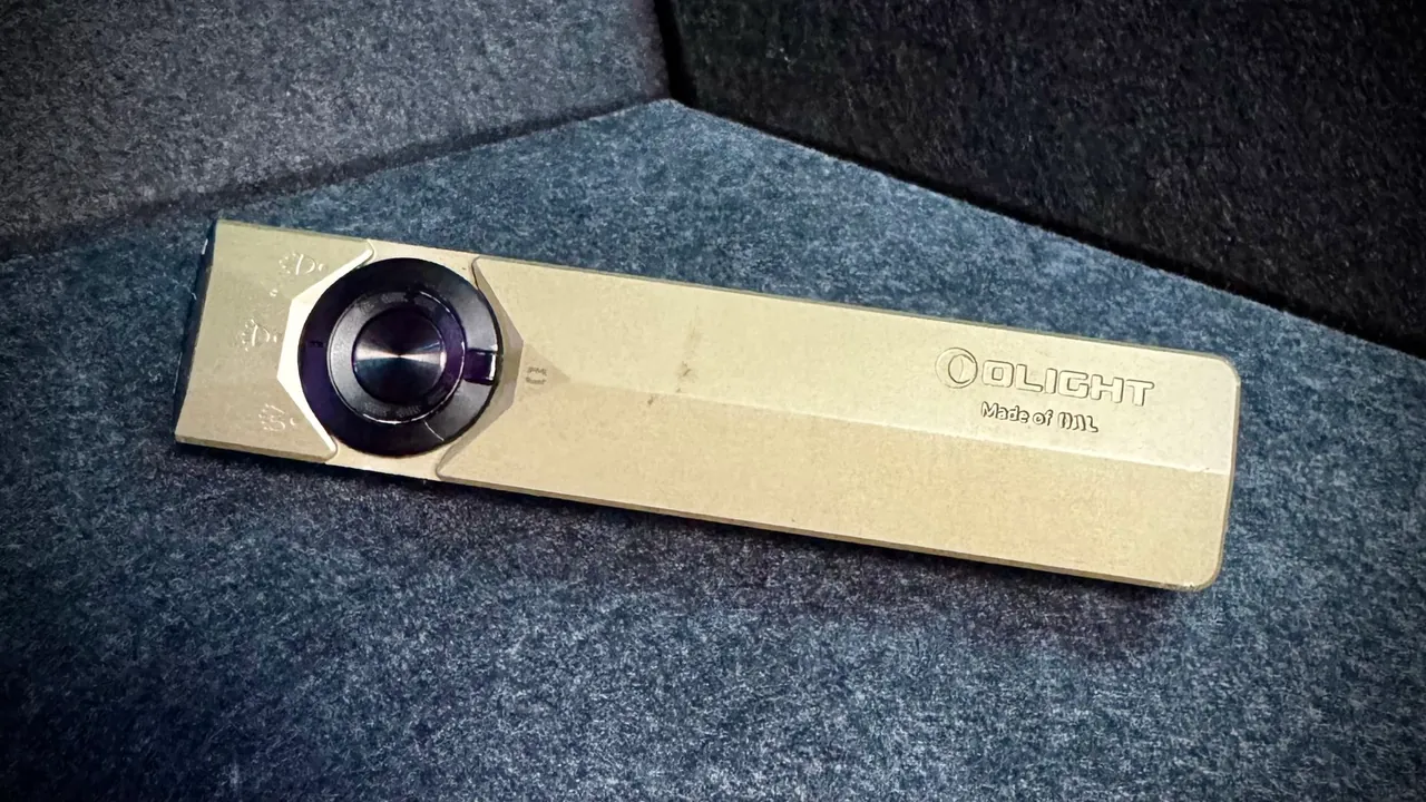 Top face of the Olight ArkPro Ultra showing the central rotary control button ringed by a green indicator, the mode icons for flood, spot and UV, the OLIGHT logo, and the 'Made of OAL' engraving on the flat O-aluminum body