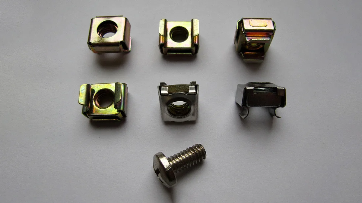 An assortment of metal cage nuts and a mounting screw laid out on a grey surface, the traditional rack fastener the Rackstuds replace