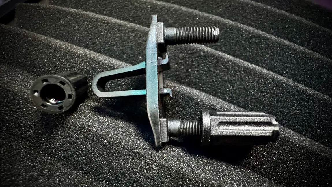 An all-black Rackstuds Duo taken apart on foam: the knurled lock nut, and the one-piece 1RU stud with its spanning bracket and threaded post, no washer