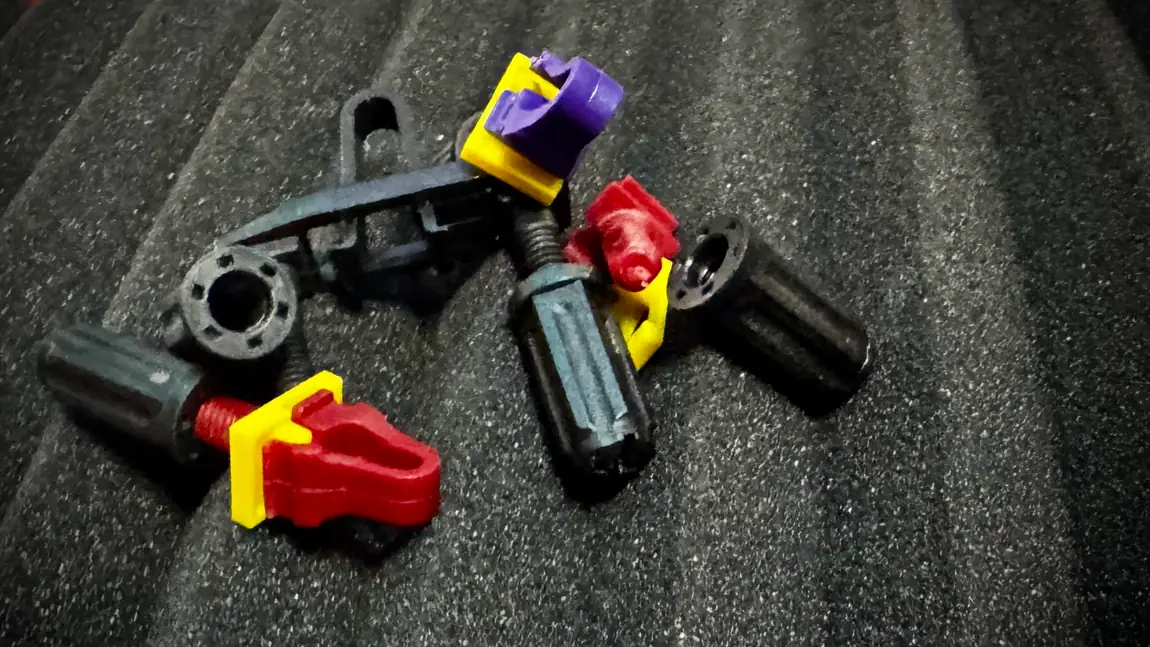 A loose handful of Rackstuds parts on foam, mixing red and purple studs, black lock nuts and yellow washers, showing both rail-thickness variants together