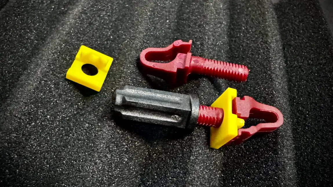 A Rackstuds Series II Red kit taken apart on foam: the yellow load-spreading washer, two red front-hook studs with threaded posts, and the black lock nut with its screwdriver slot